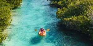 Pessoas em kayak nos Rápidos de Los Rápidos de Bacalar, rodeadas por águas cristalinas e vegetação tropical.