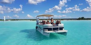 Pessoas a relaxar num barco na lagoa de Bacalar, rodeadas por águas azul-turquesa.